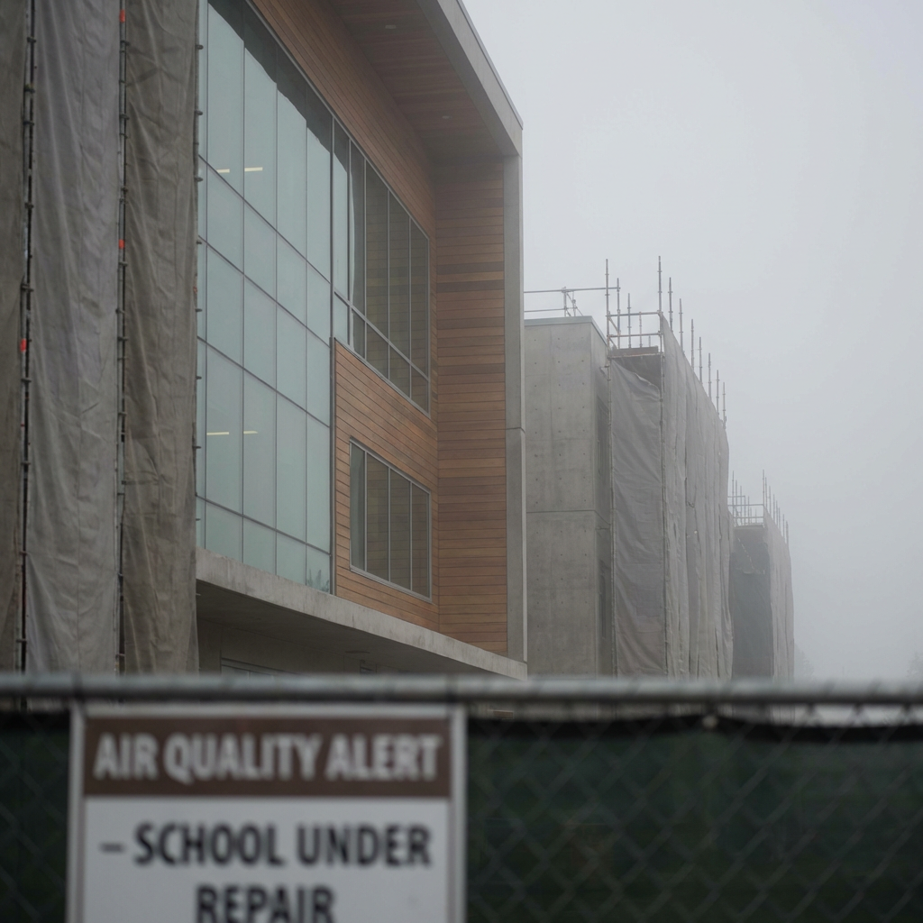 Modern school building under repair behind a fence with an AIR QUALITY ALERT sign.